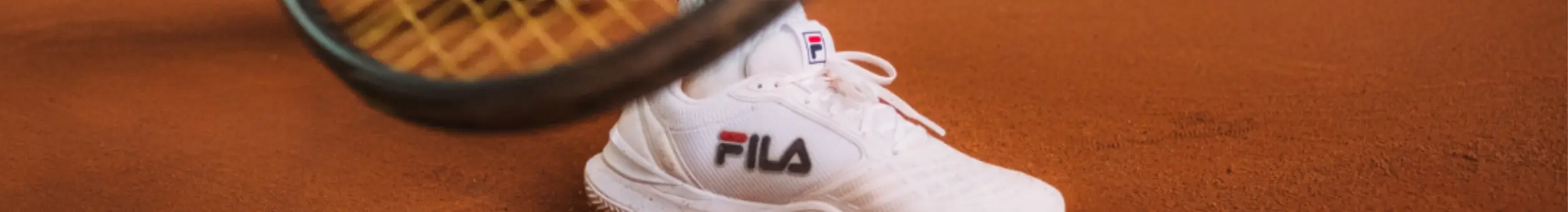 White FILA sports shoe on a clay tennis court, with a clearly visible logo.