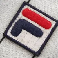 Two athletes are playing tennis on an outdoor court with a dramatic cloudy sky in the background. Both wear matching sports outfits, consisting of yellow shirts, black shorts, and tennis shoes. One player is airborne, about to hit the ball with a racket, while the other is in a defensive stance, ready to respond. The image conveys action, competition, and dynamism.